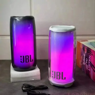 Two cylindrical portable speakers lit from inside in purple and blue, standing on a desk with a cable coiled in front