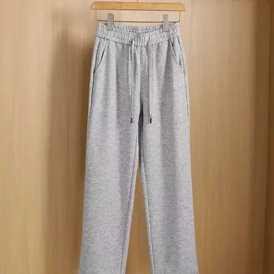 Grey marl sweatpants on a wooden hanger against a timber wall, elastic drawstring waist and side pockets visible