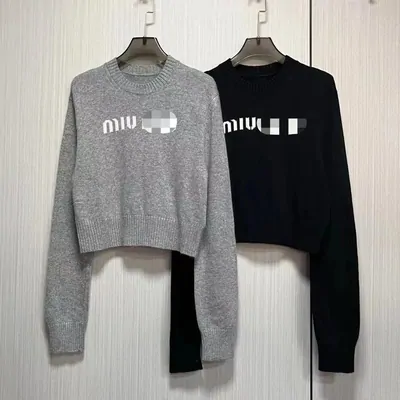 Two cropped knit jumpers on hangers, one grey and one black, each with a chest logo panel